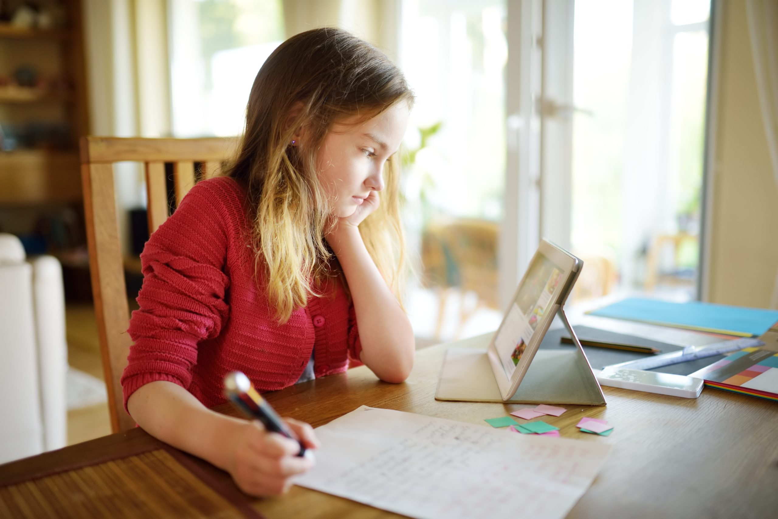Young girl in red jumper doing her homework with digital tablet at home