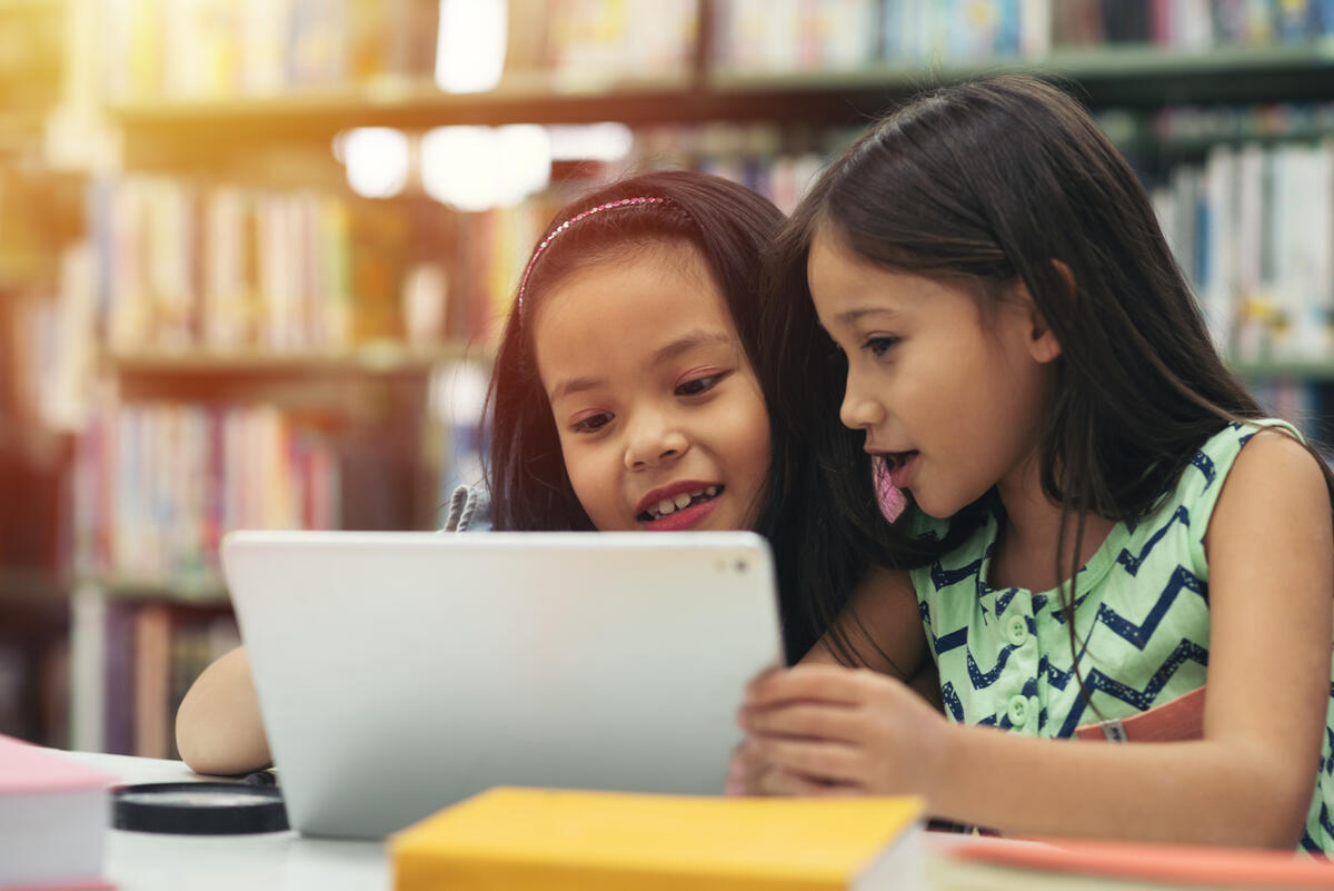 Two young girls working together on a tablet in the school library