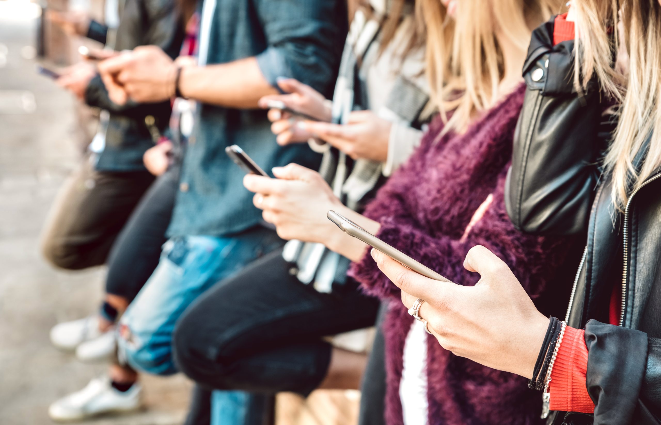 Six young people leaning against a wall and interacting with the smartphones