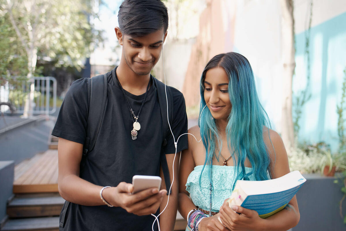 Teenagers walking together, sharing headphones and looking at the same smartphone while smiling