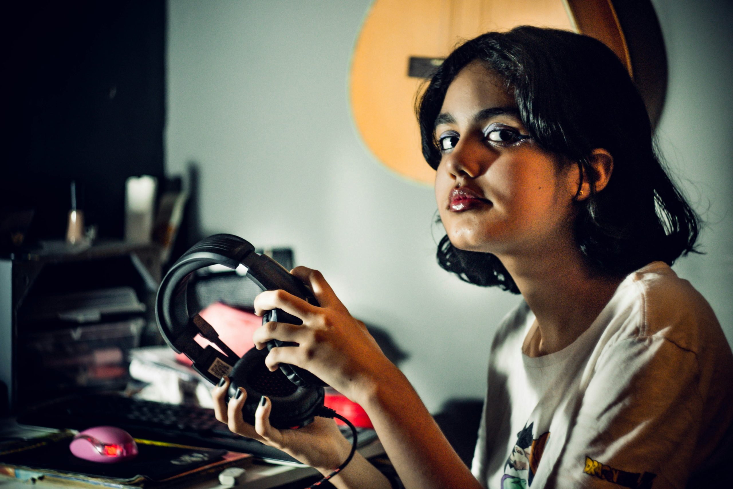 Young girl sitting at a computer desk holding a pair of over the hear headphones